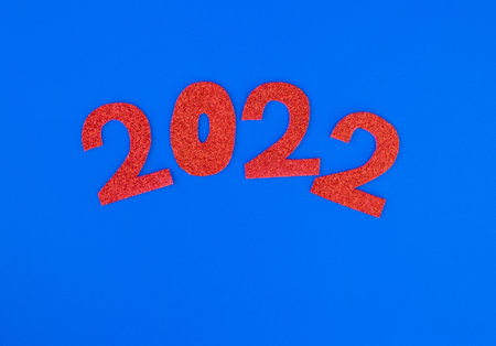 Happy New Year 2022. Christmas background with red glittering numbers 2022 close-up on blue...