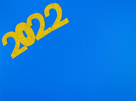 golden glittering shapes of numbers 2022 on light blue background, minimalism new year concept.