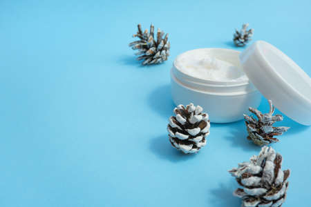Jar of cream for hands, eyes, face, and fir cones on a blue background. Set of cosmetics for skin and body care with pine needlesの写真素材
