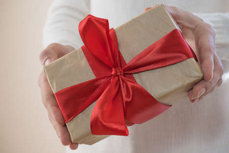 Gift with a red ribbon in female hands, giving a surprise gift box. Boxing day, holiday, birthday, christmas, mother's dayの写真素材