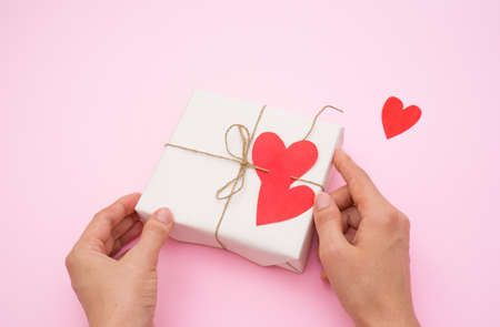girls hands preparing a gift for Valentines Day, handmade valentines and an envelope on a pink...