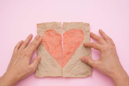 love concept - female hands stick together torn red heart on paper on pink background.の写真素材