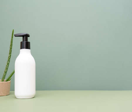 A white bottle of cream, shampoo with a black dispenser and an aloe vera flower on an earthy green background.の写真素材