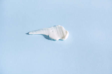 White smear of cosmetic cream on a blue background. Creamy base texture isolated. A smear of face cream. Close-up of creamy textureの写真素材