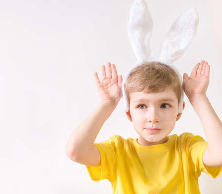 Happy child in a yellow t-shirt in rabbit ears on a white background. Happy Easter concept with...