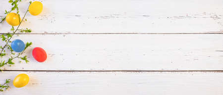 Banner of colorful Easter eggs with spring bloom flowers and green leaves, on a white wooden background. Space for textの写真素材