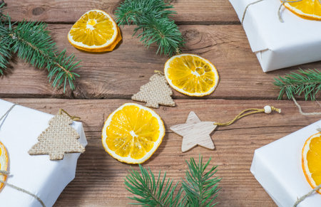 Christmas presents or gift box wrapped in kraft paper with decorations, pine cones, dry orange orange slices and fir branches on a rustic wooden background. Holiday concept.の写真素材
