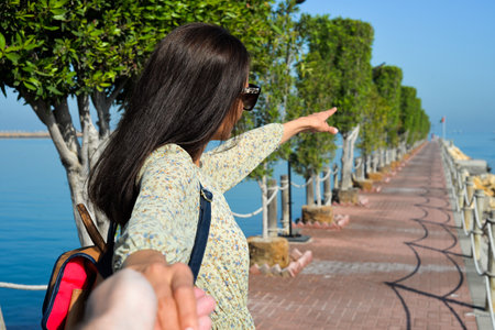 A young woman in a dress points the direction to the sea with her hand. Pier at the beach of Sharjah...