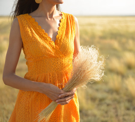 Close-up of a woman in an orange dress with a bouquet of field grass in a field at sunsetの写真素材