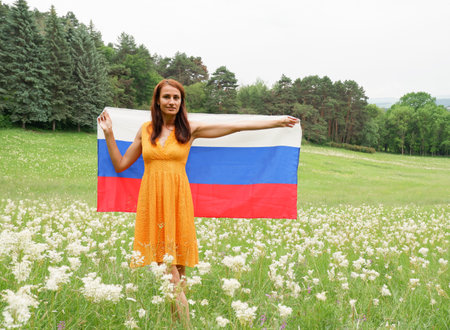 Young woman in a yellow dress with the national flag of Russia outdoors in a flowering fieldの写真素材