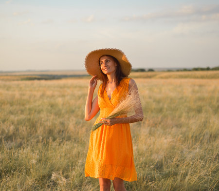 Beauty girl outdoors enjoying nature. A beautiful girl in an orange dress and a straw hat enjoys the sunset.の写真素材