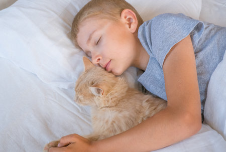 A child in bed cannot fall asleep, yawns, grimaces and plays with a ginger catの写真素材