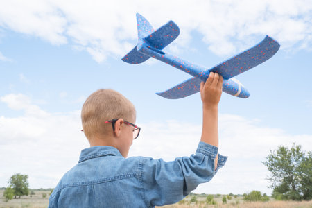 Portrait of a happy child playing with a toy airplane against a blue sky in an open field.の写真素材