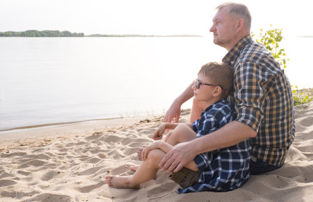 Father's day concept. Father and son sit together on the river bank and look into the distanceの写真素材