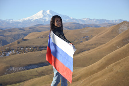 A young brunette woman stands against the backdrop of the snow-capped Mount Elbrus, looking at the...