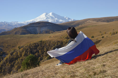 A young brunette woman sits on a stone and looks at the mountains around, her shoulders are covered...
