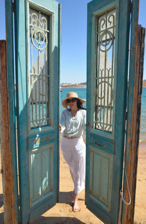 Young woman opens wooden wooden doors overlooking the sea.の写真素材