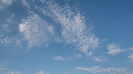 Blue sky with scattered white cirrus clouds. The clouds vary in size and shape, creating a serene...