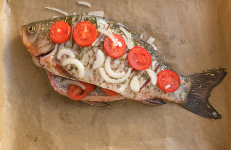 Fresh whole river crucian fish on parchment with tomatoes and spices ready for baking.の写真素材