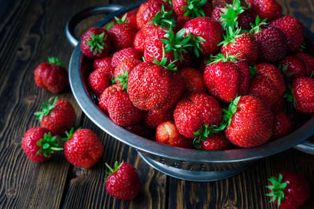 Colander with fresh strawberry and lying strawberry on wooden backgroundの写真素材