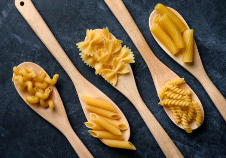 Various types of pasta on black background. Pasta in wooden spoons.の写真素材