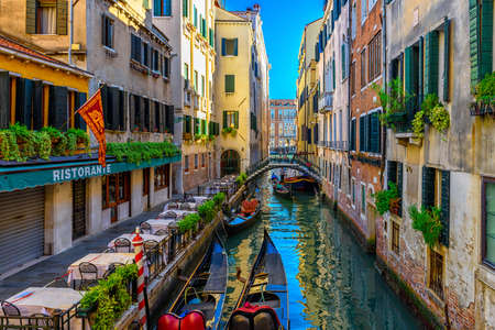 Narrow canal with gondola and tables of restaurant in Venice, Italy. Architecture and landmark of Venice. Cozy cityscape of Venice.の写真素材