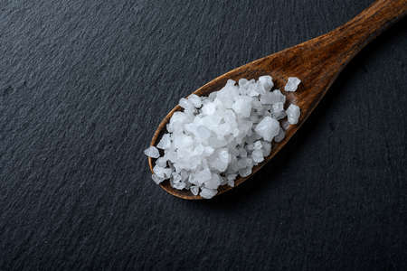 Sea salt in a wooden spoon on a black background. Coarse salt. top view.の写真素材
