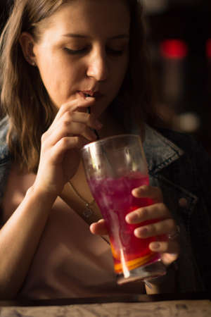 Portrait of pretty smiling young woman with fruit cocktail in barの写真素材
