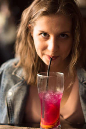 Portrait of pretty smiling young woman with fruit cocktail in barの写真素材