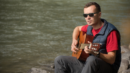playing the guitar on the background of glare from the water