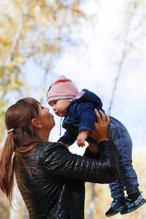 Young mother with a small child in the autumn park. A beautiful woman is spinning with her little...