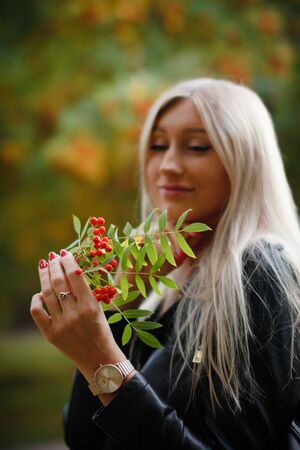 Portrait of a beautiful young woman who enjoys autumn while walking around the city. Attractive blonde in a black leather jacket on a background of autumn treesの写真素材