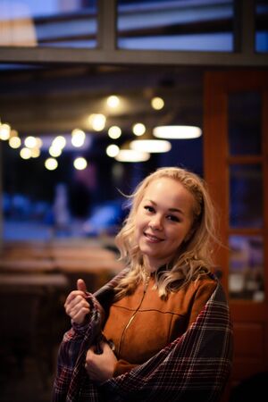 Young pretty blonde with a plaid on her shoulders on a cozy terrace on Christmas evening. Cozy autumn evening.の写真素材