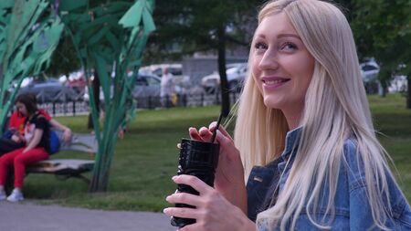 Beautiful blonde is talking on the phone during a lunch in a cafe. She smiles. Young woman with a smartphone in her hands in a summer cafe.の写真素材