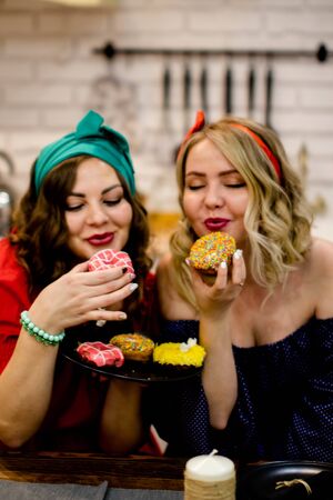 Two women bite tasty donuts during a diet.の写真素材