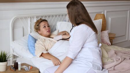 Doctor and patient healthcare concept. A woman doctor in a white medical coat sits on the bed of a sick woman and advises her. Ambulance concept. Personal doctor.の写真素材