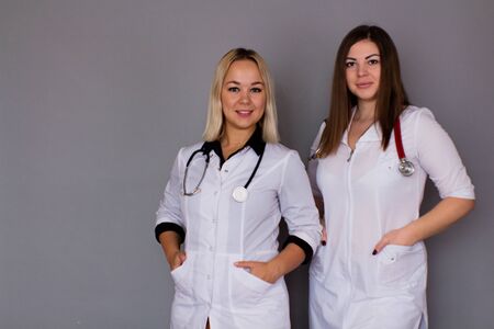 Two women doctor in white medical coats on a gray background. Healthcare conceptの写真素材
