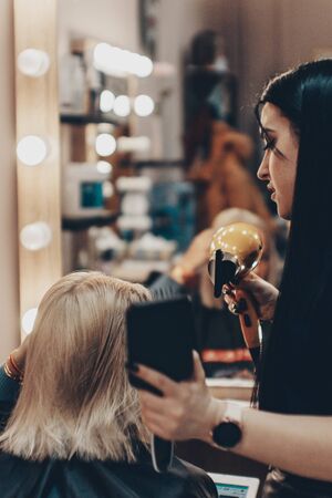 Beautiful young woman hairdresser giving new haircut to female client at salonの写真素材
