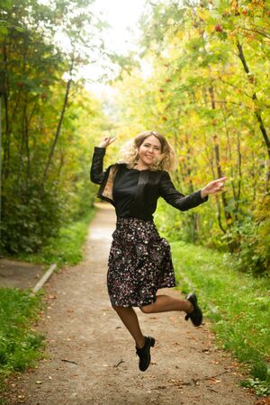 Beautiful young woman is enjoying autumn while walking in a park. Attractive blonde in a black...