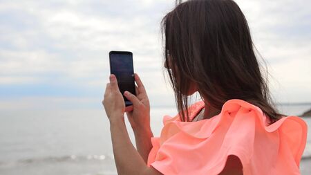 Young woman shoots a video with sunset at sea on her smartphone