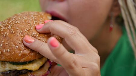 Pretty young woman is eating appetizing hamburger on the street. Close-upの写真素材