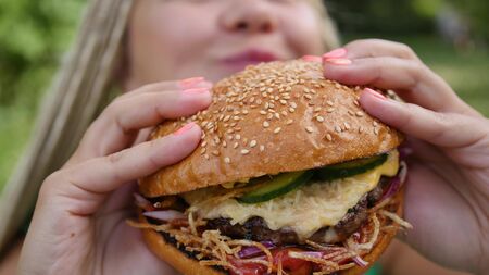 Pretty young woman is eating appetizing hamburger on the street. Close-up