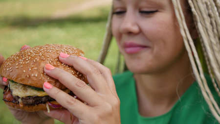 Pretty young woman is eating appetizing hamburger on the street. Close-upの写真素材