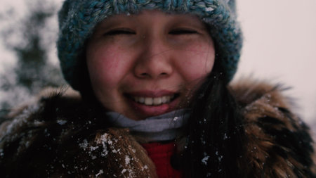 Beautiful young Asian woman in a warm winter hat laughs on the background of the winter forest. Blurred background. Close up. Winter holidays concept.の写真素材