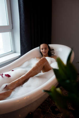 Young beautiful woman relaxing while listening to music in wireless headphones in bubble bath.の写真素材
