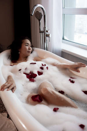 Young beautiful woman relaxing while listening to music in wireless headphones in bubble bath.の写真素材