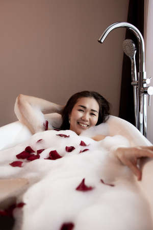 Young beautiful woman relaxing while listening to music in wireless headphones in bubble bath.