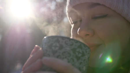 Attractive young beautiful woman walks in the winter snowy forest and drinks hot tea, coffee from a mug. Portrait of a happy girl in the winter forest. Lifestyle, happiness, vacation conceptの写真素材
