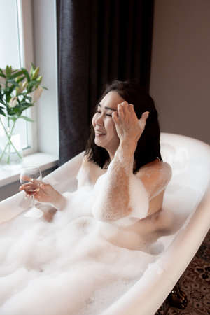 The relaxed woman touches the skin in lather with lather. Woman taking a bath at homeの写真素材