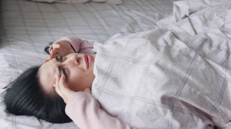 Young woman in pink pajamas suffering from headache while lying in her bed